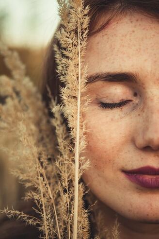 Picture of a woman reflecting with her eyes closed and wheat near her lips, boho style
